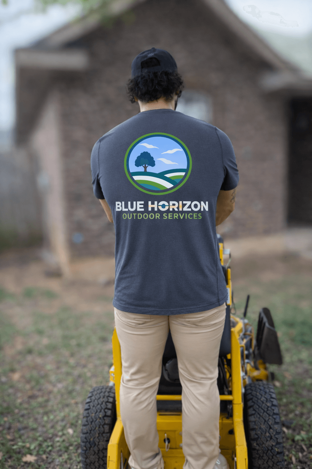 Man wearing a Blue Horizon Outdoor Services shirt stands behind a yellow lawn mower.